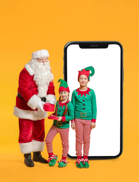 Joulupukki ja pikku tontut lahja ja iso matkapuhelin keltaisella taustalla - Valokuva, kuva