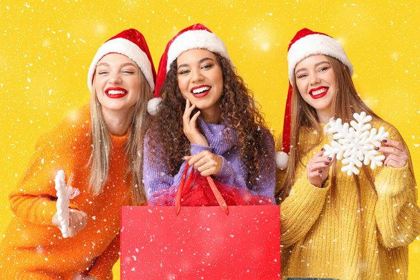 Gyönyörű fiatal nők a Mikulás kalapok, hópelyhek és bevásárló táska sárga háttér - Fotó, kép