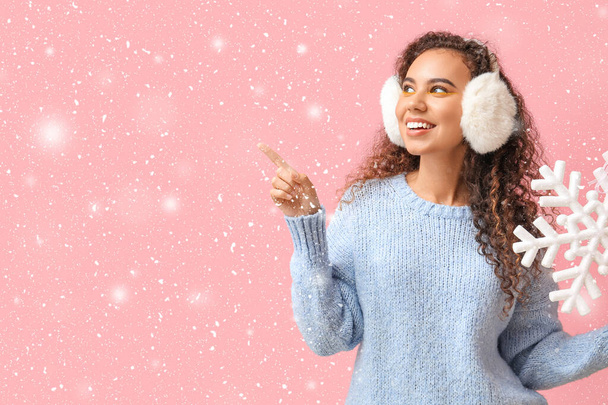 Beautiful African-American woman with big snowflake pointing at something on pink background - Photo, Image