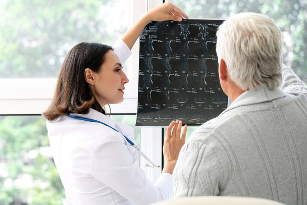 Doctora que muestra radiografía a paciente mayor en consultorio médico - Foto, imagen