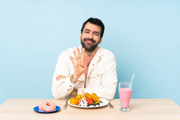 Мужчина за столом, завтракающий вафлями и молочный коктейль счастливый и считает четверых с пальцами - Фото, изображение