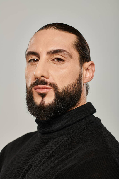 retrato de hombre árabe masculino con barba posando en cuello alto negro sobre fondo gris - Foto, Imagen