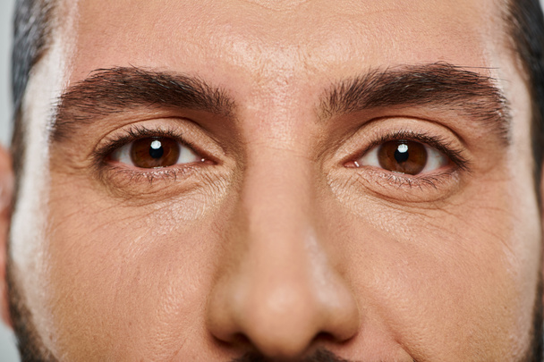 primer plano plano del hombre árabe de ojos marrones mirando la cámara g sobre fondo gris, parte de la cara - Foto, Imagen