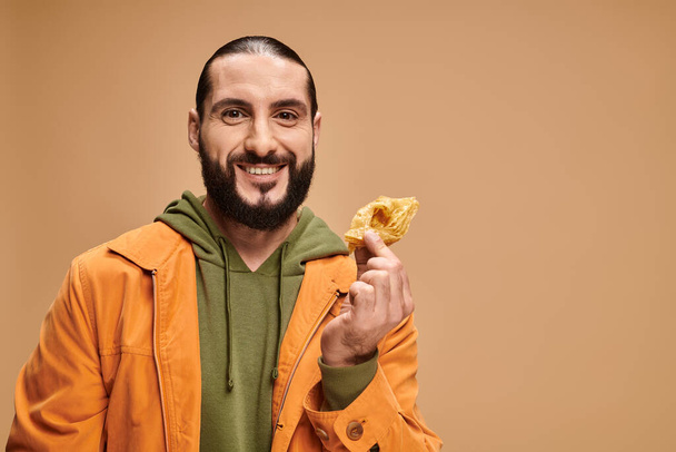 glücklicher Mann hält Honig-Baklava in der Hand und blickt in die Kamera auf beige, traditionelles mittelöstliches Dessert - Foto, Bild