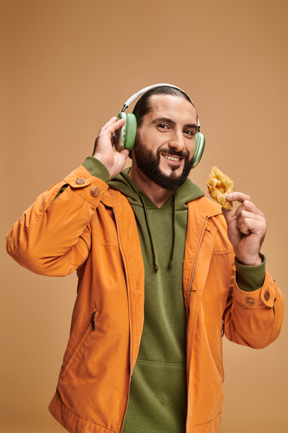 hombre árabe feliz en auriculares con miel baklava sobre fondo beige, postre del Medio Oriente - Foto, imagen