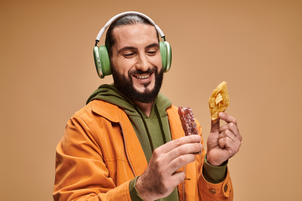 happy man in headphones holding two middle eastern desserts, honey baklava and churchkhela - Photo, Image