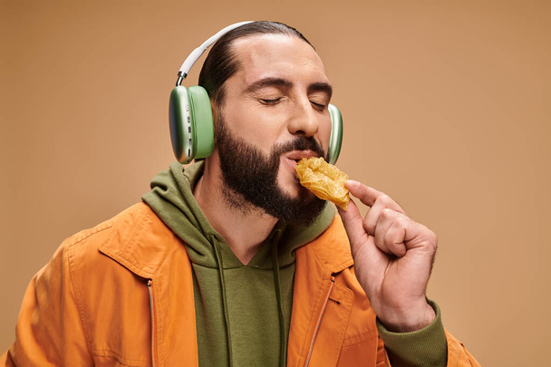 gelukkig man in hoofdtelefoon eten heerlijke honing baklava op beige achtergrond, turkse lekkernijen - Foto, afbeelding