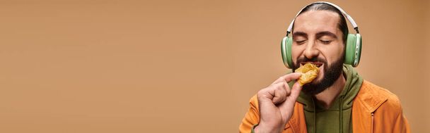 vrolijk man in hoofdtelefoon eten heerlijke honing baklava op beige achtergrond, turkse lekkernijen banner - Foto, afbeelding