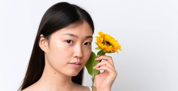 Junge Chinesin isoliert auf weißem Hintergrund mit einer Sonnenblume. Porträt aus nächster Nähe - Foto, Bild