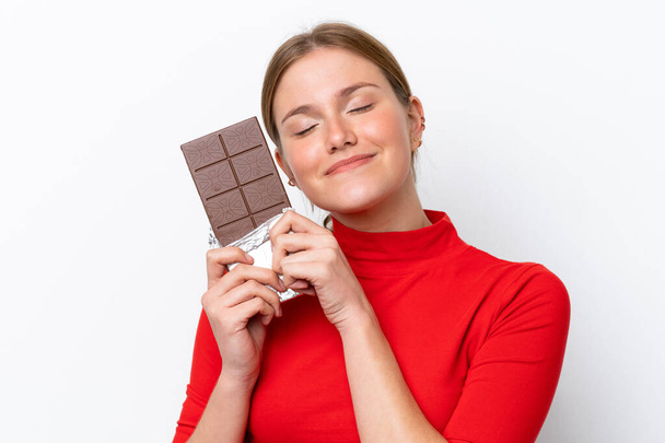 Mujer joven caucásica aislada sobre fondo blanco tomando una tableta de chocolate y feliz
 - Foto, imagen