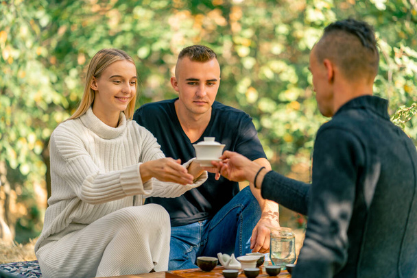 Un maestro del tè professionista passa una tazza di tè coperta con un coperchio a una giovane coppia sorridente per la degustazione. - Foto, immagini