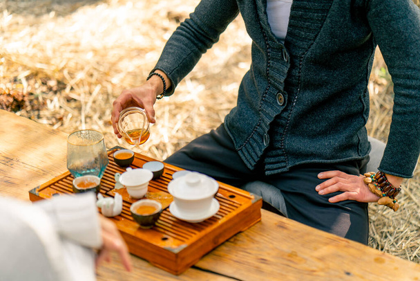 Las manos de un maestro de té profesional que vierte té verde natural fresco de una tetera de vidrio en cuencos en una mesa de madera chaban - Foto, Imagen
