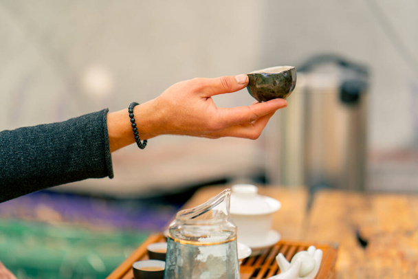 Close-up shot van de hand van een theemeester die een kom natuurlijke thee aan een meisje geeft bij een theeceremonie - Foto, afbeelding