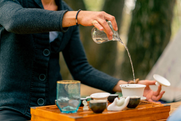 Die Hand eines Mannes gießt bei einer Teezeremonie kochendes Wasser in Keramikschalen, um Tee zu kochen. - Foto, Bild