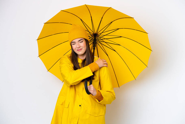 Giovane donna brasiliana con impermeabile e ombrello isolato su sfondo bianco che soffre di dolore alla spalla per aver fatto uno sforzo - Foto, immagini