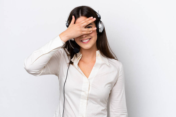 Telemarketer mujer caucásica trabajando con un auricular aislado sobre fondo blanco cubriendo los ojos con las manos y sonriendo - Foto, imagen