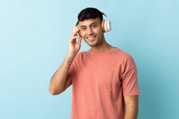 Νεαρός Κολομβιανός απομονωμένος σε μπλε φόντο ακούγοντας μουσική - Φωτογραφία, εικόνα