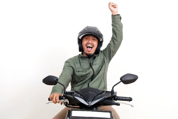 Izgatott ázsiai férfi motorozik, miközben ökölbe szorítja a kezét. Fehér alapon elszigetelve - Fotó, kép