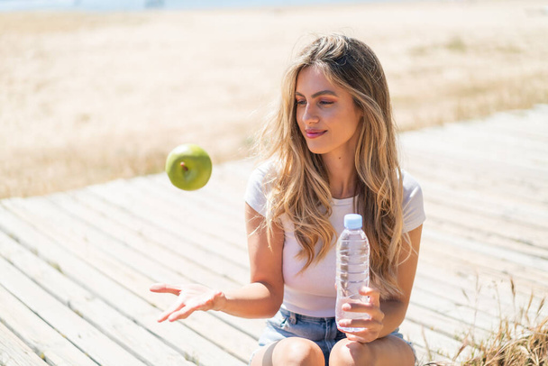 Kaunis blondi Uruguayn nainen omena ja pullo vettä - Valokuva, kuva
