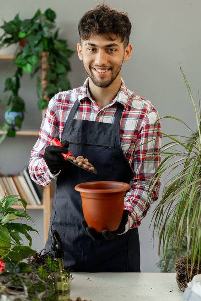 Portrait of Arabic man transplanting a plant into a new pot at home, pouring drainage. Spring care for houseplant. Copy space - Photo, Image