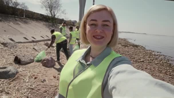 Vista panorámica de una voluntaria ambiental mirando la cámara y hablando mientras filma vlog o videollamadas durante la limpieza de la costa - Imágenes, Vídeo