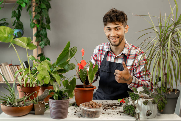 Hymyilevä arabialainen mies kantaa vihreitä kasveja kotona. Onnellinen mies puutarhuri tai kukkakauppias huolehtia kotimaisia kukkia. Puutarhanhoito käsite. Kopioi tila - Valokuva, kuva