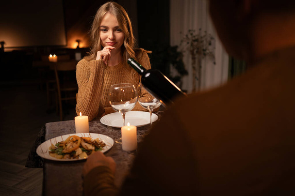 Romantic couple dining together over candlelight during romantic dinner, man pouring red wine in wineglasses, celebrating Valentines Day. Copy space - Photo, Image