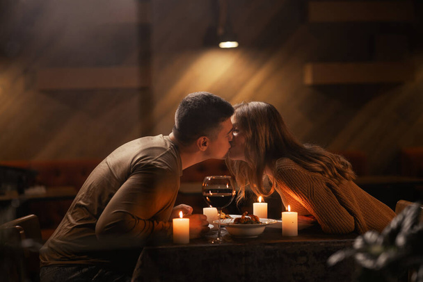 Happy young couple in love kissing, drinking red wine having romantic dinner, celebrating Valentines day, anniversary, sitting at home. Copy space - Photo, Image
