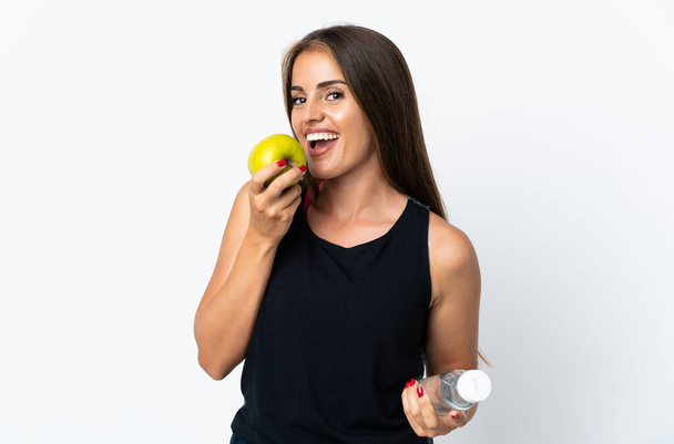 Jonge Uruguayaanse vrouw geïsoleerd op witte achtergrond met een fles water en het eten van een appel - Foto, afbeelding