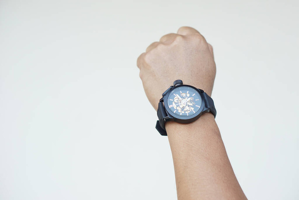 Cerca de mano hombre lleva reloj negro contra fondo gris de la pared. Concepto, accesorio de moda para contar el tiempo, te hacen lucir elegante, puntual e inteligente. Reloj de pulsera analógico.     - Foto, imagen