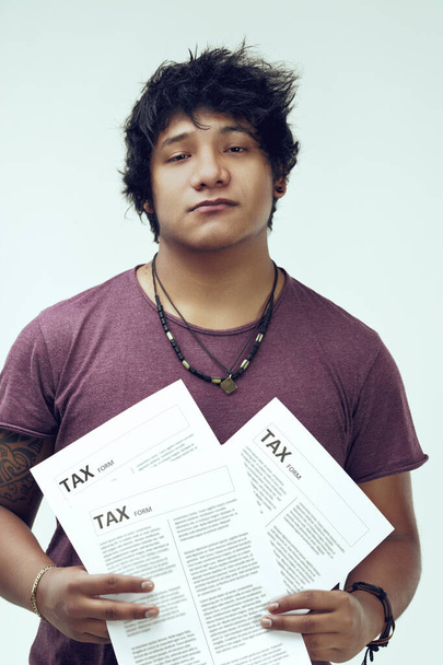 С налоговыми документами молодой скучающий мужчина носит уникальное ожерелье, чистую татуировку и бордовый топ. Их черные волосы добавляют характерный оттенок - Фото, изображение