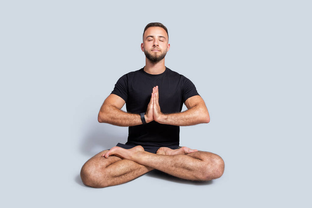 Ruhige junge kaukasische Mann mit Bart in Sportbekleidung Praxis Yoga in Lotusposition, genießen Atemübungen, Ruhe, isoliert auf grauen Studiohintergrund, volle Länge. Training und Gesundheitsfürsorge - Foto, Bild