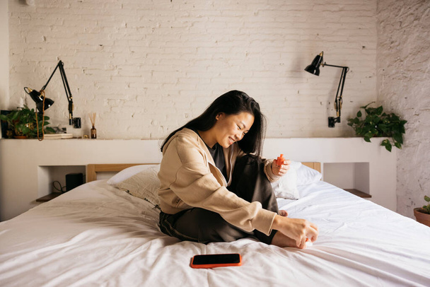 Jeune femme chinoise gaie faisant pédicure sur le lit à la maison - Photo, image