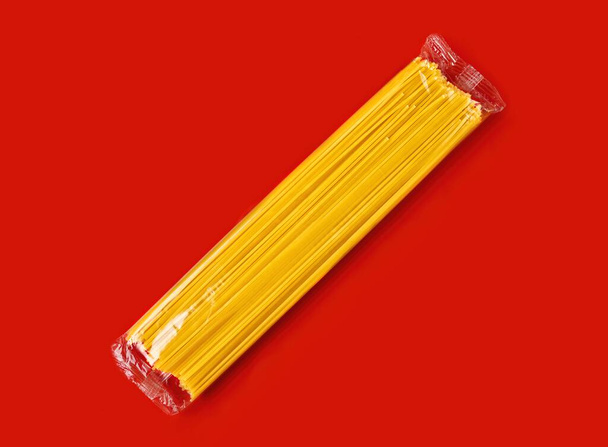 Makaron spaghetti w plastikowym opakowaniu izolowanym na czerwonym tle. - Zdjęcie, obraz