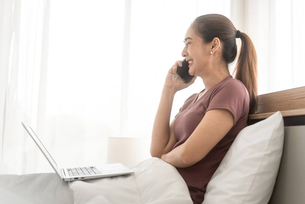 Lifestyle-Routine mit Internet-Technologie-Konzept. Junge erwachsene asiatische Frau im Gespräch mit Smartphone auf dem Bett für telemedizinische psychische Gesundheit. Menschen ruhen sich im Schlafzimmer aus. - Foto, Bild