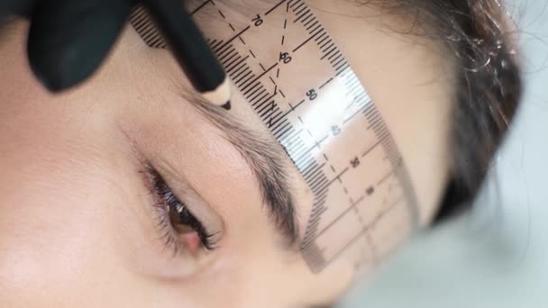 Mikrobleyding Augenbrauen Workflow in einem Schönheitssalon. Eine Frau in Handschuhen bereitet sich mit einem Lineal auf ein dauerhaftes Augenbrauen-Make-up vor. Nahaufnahme. - Filmmaterial, Video