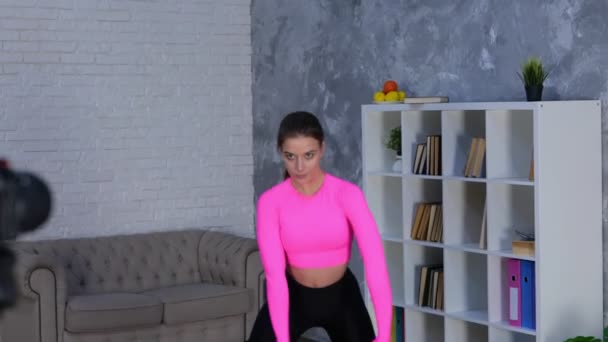 Active athlete young lady warming up, doing legs stretching exercises at home while using camera on tripod and recording sports video for vlog. Home fitness, workout concept. Real time video. - Footage, Video