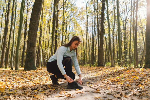 Tyttö sitoo kengännauhansa. Kaunis tyttö tekee kunto luonnossa aurinkoisella syksyllä metsässä. Keho positiivinen, urheilu naisille, harmonia, terveellinen elämäntapa, itserakkaus ja hyvinvointi. - Valokuva, kuva