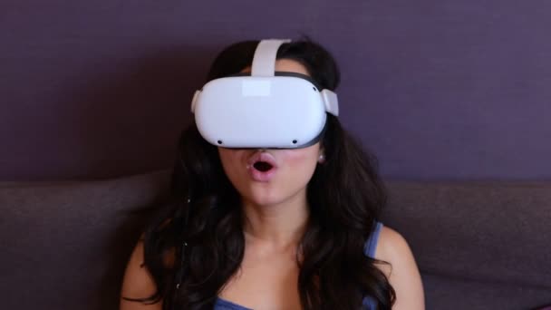 Налякана красива жінка, використовуючи гарнітуру VR, дивлячись у віртуальну реальність, сидить на ліжку вдома. Сучасна концепція технології. Відео в реальному часі. - Кадри, відео