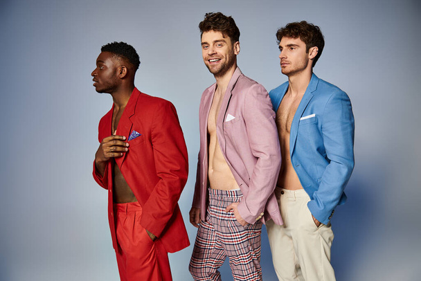 allegro attraente diversi uomini in abiti vibranti alla moda in posa in un unico file su sfondo grigio - Foto, immagini