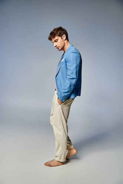 mladý pohledný muž v pulzujícím rozepnutém modrém saku pózující na šedém pozadí, módní koncept - Fotografie, Obrázek
