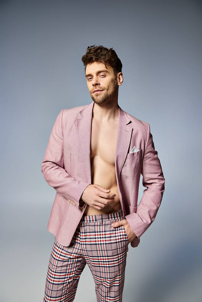 bel homme en costume rose vif déboutonné posant allègrement sur fond gris, concept de mode - Photo, image