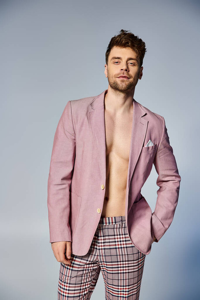knappe stijlvolle man in ongeknoopte levendige roze pak poseren verleidelijk op grijze achtergrond, mode - Foto, afbeelding