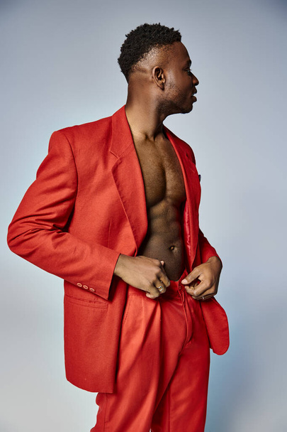 aantrekkelijk Afrikaans amerikaanse man in levendige rode kleding die op grijze achtergrond, mode concept - Foto, afbeelding