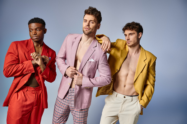 alluring sexy diverse men in unbuttoned vibrant suits posing on gray backdrop, fashion concept - Photo, Image