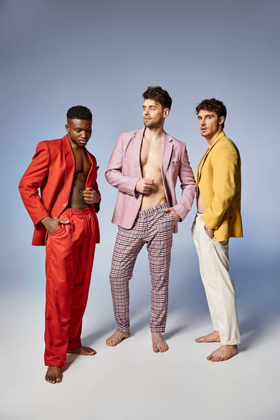handsome multiracial friends in unbuttoned bright suits on gray background, fashion concept - Photo, Image