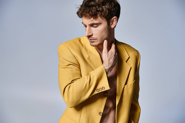 attrayant jeune homme en veste jaune élégant posant attrayant sur fond gris, concept de mode - Photo, image
