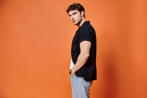 appealing stylish man in casual outfit on orange backdrop looking at camera, fashion concept - Photo, Image