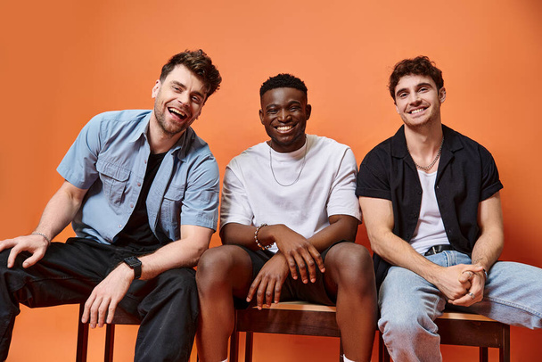 cheerful diverse men in casual street outfits smiling happily on orange backdrop, fashion concept - 写真・画像