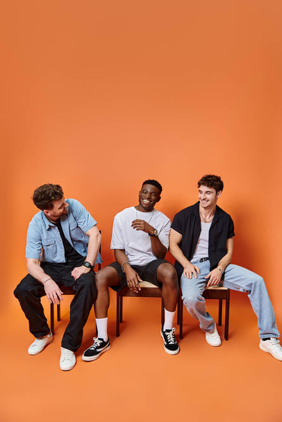 fröhliche gemischtrassige Männer in lässigen urbanen Outfits, glücklich lächelnd auf orangefarbenem Hintergrund, Modekonzept - Foto, Bild